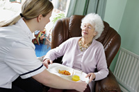A personal care assistant helping with food preparation for an elderly woman at home