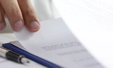 A hand lifts up a piece of paper with a pen next to it
