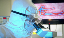 A scientist wearing PPE looks through a microscope
