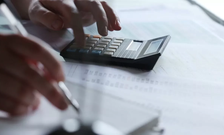 Two hands, one typing in a calculator while the other writes with a pen on paper